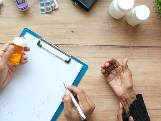 Healthcare professional organising medication on a table, beside an older person's hands.