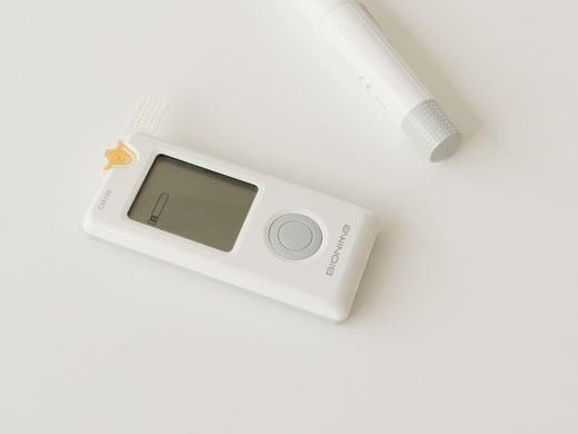 Blood glucose meter and lancet resting on a light surface.